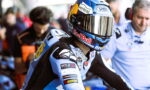 MotoGP rider in a blue racing suit wearing a helmet with Red Bull and Shoei logos, in the pit area.