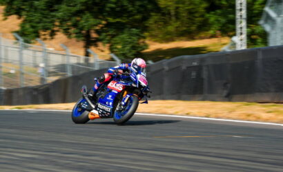 Motorcycle racer in blue gear leans into a turn on a race track.