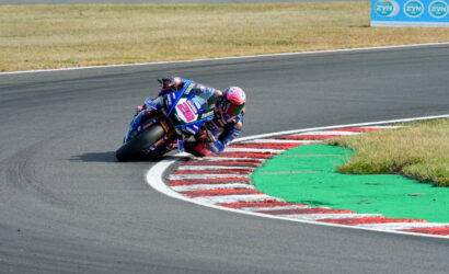Moto racing rider on a blue Yamaha motorcycle leans into a sharp right-hand curve on a race track, wheels near painted curbs.