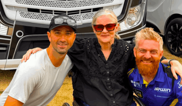 Three people posing together in front of a large truck, smiling at the camera.