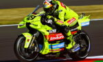 Racing motorbike in neon yellow livery leaning into a track bend with a helmeted rider in matching gear, sponsors visible on bike sides and fairings.