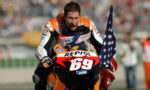 MotoGP rider in orange Repsol suit on a bike #69 celebrates, waving an American flag.
