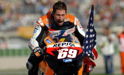 MotoGP rider in orange Repsol suit on a bike #69 celebrates, waving an American flag.