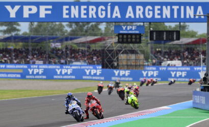 Motorcycle race on a track with riders in colorful leathers, blue YPF banners above and along the sidelines in Argentina.