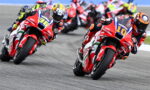 Motorcycle race: red racing bikes lean into a curve with racers in full gear, numbers 10 and 36 visible at the front.