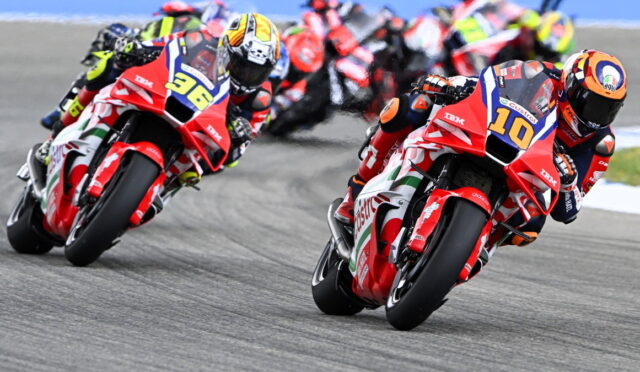 Motorcycle race: red racing bikes lean into a curve with racers in full gear, numbers 10 and 36 visible at the front.