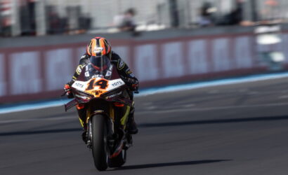 Motorcycle racer wearing an orange helmet on a black-and-orange racing bike, number 14, speeding on a track.