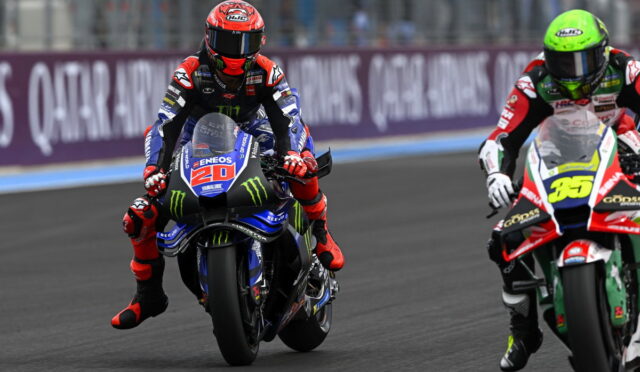 Two motorcycle racers wheel-to-wheel on a race track, front bike number 20 wearing blue and red with Monster energy graphics.
