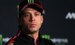 Athlete wearing a black cap with red trim and Monster logo at a press conference with a dark backdrop.