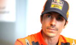 Close-up of a man wearing a Red Bull KTM cap and orange racing suit, looking slightly to the right.