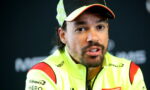 Close-up of a man in a neon yellow racing jacket and cap, speaking at a press conference.