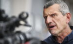 Man with gray hair speaks into a microphone during an interview, camera blurred in the foreground