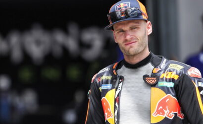 Moto racer in a KTM/Red Bull racing suit, looking at the camera outdoors.