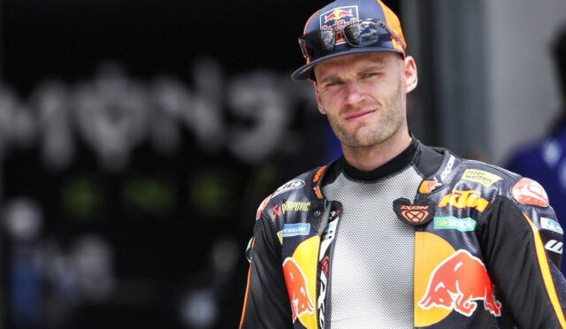 Moto racer in a KTM/Red Bull racing suit, looking at the camera outdoors.