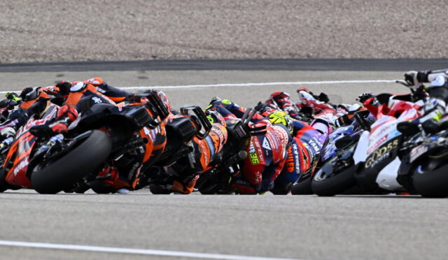 Pack of motorcycle racers leaning into a tight turn on a race track.