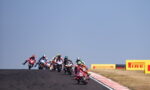 Group of motorcycle racers lean into a track bend on a racetrack with Pirelli barriers in the background.