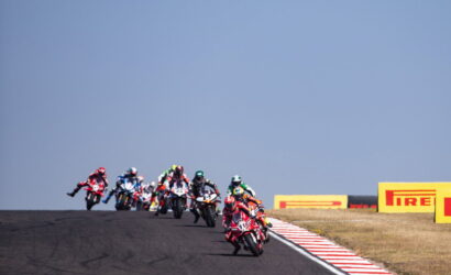Group of motorcycle racers lean into a track bend on a racetrack with Pirelli barriers in the background.
