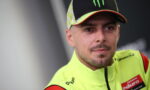 Racer in bright neon-yellow racing suit and cap, with Monster logo, looking to the side with a neutral expression.