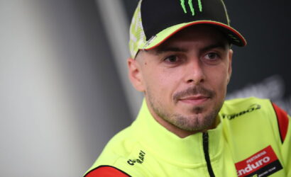 Racer in bright neon-yellow racing suit and cap, with Monster logo, looking to the side with a neutral expression.