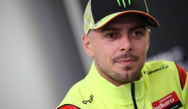 Racer in bright neon-yellow racing suit and cap, with Monster logo, looking to the side with a neutral expression.
