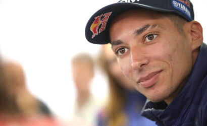 Close-up of a young man wearing a navy cap with Red Bull and sponsor logos, looking at the camera.