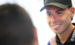 Young man in a black Yamaha cap and lanyard smiles while talking to someone off-camera.