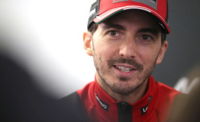 Close-up of a man in a red racing cap and jacket smiling at the camera.