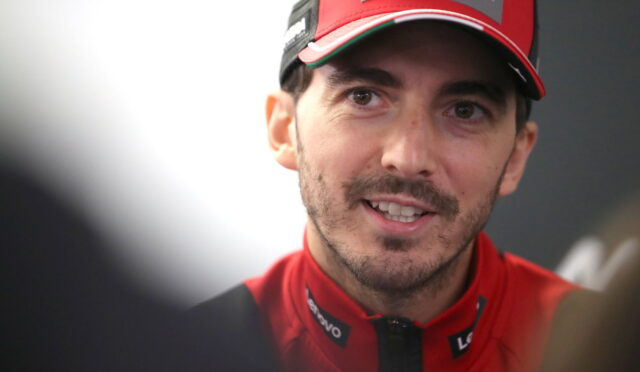 Close-up of a man in a red racing cap and jacket smiling at the camera.