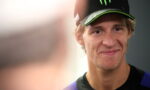 Portrait of a smiling young man wearing a black cap with a green Monster energy logo and a dark athletic shirt.