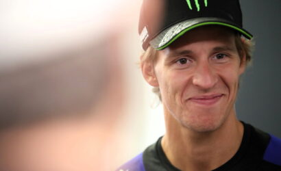 Portrait of a smiling young man wearing a black cap with a green Monster energy logo and a dark athletic shirt.