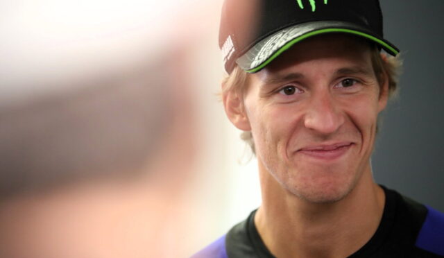 Portrait of a smiling young man wearing a black cap with a green Monster energy logo and a dark athletic shirt.