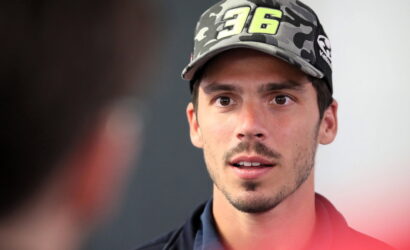 Close-up of a young man wearing a camouflage cap with the number 96, speaking to someone off-screen.
