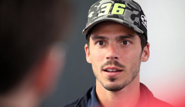 Close-up of a young man wearing a camouflage cap with the number 96, speaking to someone off-screen.