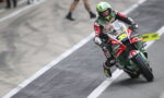 Moto racer in red, white, and green leans into a left turn on a race track, number 35 visible on the bike's front.