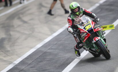 Moto racer in red, white, and green leans into a left turn on a race track, number 35 visible on the bike's front.