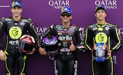 Three motorcycle racers in black and neon suits pose with helmets against a purple Qatar Airways backdrop, at a race event.