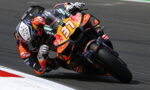 MotoGP rider in orange gear leans into a left turn on a race track; bike #37 with Red Bull branding.