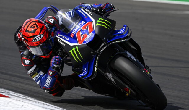Racing motorcycle leaning into a left-hand turn, rider in blue and black suit on a Yamaha bike with Monster Energy logos and the number 46 visible on the fairing, track surface blurred in the background.