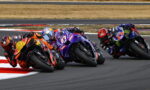 MotoGP race: four riders leaning into a tight turn on a race track, colorful sponsor-laden bikes in close proximity.