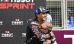 Two motorcyclists embrace in a congratulatory hug at a Tissot Sprint event, with branding in the background.