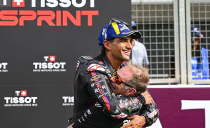 Two motorcyclists embrace in a congratulatory hug at a Tissot Sprint event, with branding in the background.