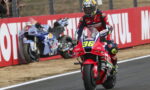 Motorcycle racer on a red racing bike #96 speeding along a track with red barrier advertising in the background.