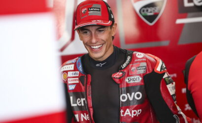 MotoGP rider in a red Lenovo Ducati racing suit smiling in the paddock/garage area.