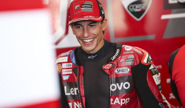 MotoGP rider in a red Lenovo Ducati racing suit smiling in the paddock/garage area.
