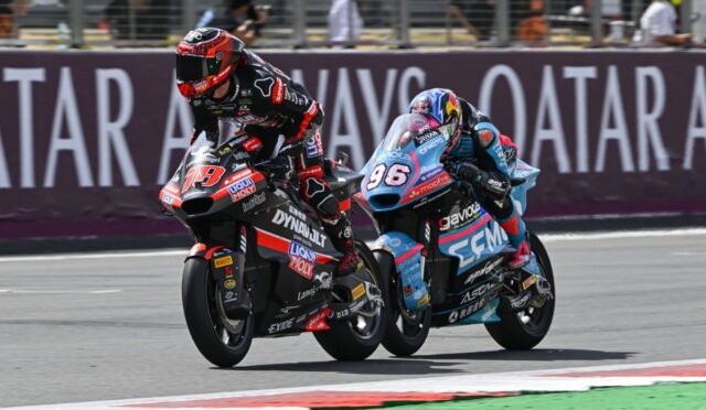 Two professional motorcycle racers lean into a corner on a race track, colorful sponsor-labeled bikes side by side.