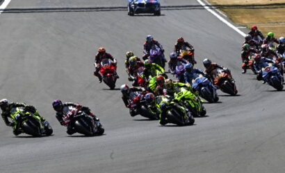 Group of motorcycle racers leaning into a turn on a race track, tightly packed and speeding through the corner.