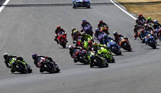 Group of motorcycle racers leaning into a turn on a race track, tightly packed and speeding through the corner.