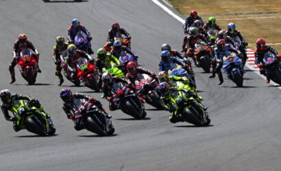 Group of motorcycle racers leaning into a turn on a racetrack with colorful leathers and bikes.