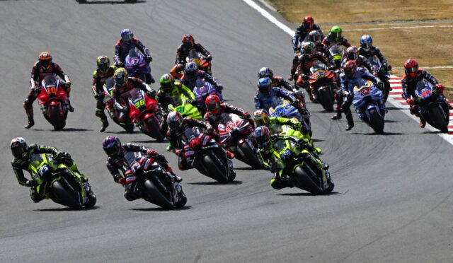 Group of motorcycle racers leaning into a turn on a racetrack with colorful leathers and bikes.