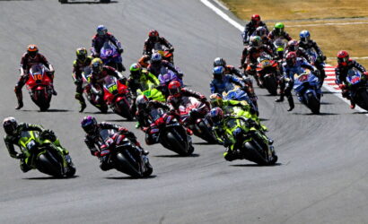 Group of motorcycle racers leaning into a sharp turn on a racetrack, wearing bright colorful gear and helmets